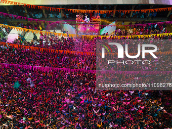 Thousands of devotees are cheering as a priest sprays colored powder and water on them during the celebrations of the colorful Holi festival...