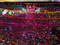 Thousands of devotees are cheering as a priest sprays colored powder and water on them during the celebrations of the colorful Holi festival...