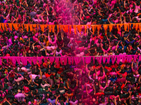 Thousands of devotees are cheering as a priest sprays colored powder and water on them during the celebrations of the colorful Holi festival...