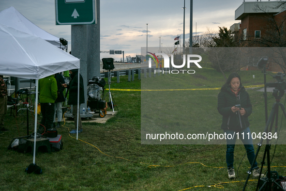 The collapsed Francis Scott Key Bridge is seen beyond a reporter at a media staging area at the Maryland Tansportation Authority headquarter...