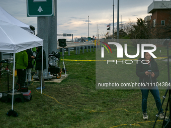 The collapsed Francis Scott Key Bridge is seen beyond a reporter at a media staging area at the Maryland Tansportation Authority headquarter...