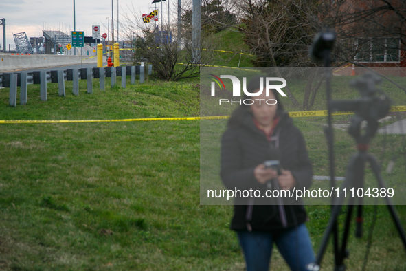 The collapsed Francis Scott Key Bridge is seen beyond a reporter at a media staging area at the Maryland Tansportation Authority headquarter...