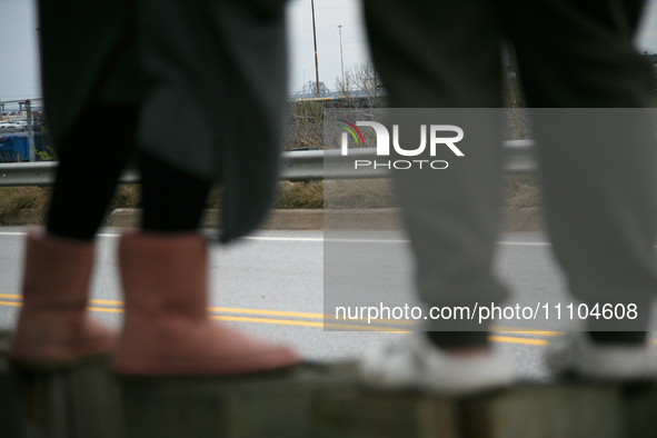 The collapsed Francis Scott Key Bridge is seen beyond the feet of people viewing the bridge from the Broening Highway in Dundalk, Maryland o...