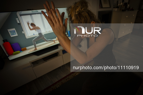 A woman is seen doing yoga exercises with YouTube trainer on a television in her living room in Warsaw, Poland on 23 March, 2024. 