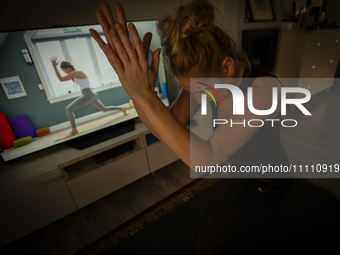 A woman is seen doing yoga exercises with YouTube trainer on a television in her living room in Warsaw, Poland on 23 March, 2024. (