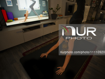 A woman is seen doing yoga exercises with YouTube trainer on a television in her living room in Warsaw, Poland on 23 March, 2024. (