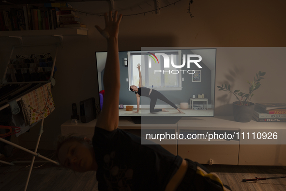 A woman is seen doing yoga exercises with YouTube trainer on a television in her living room in Warsaw, Poland on 23 March, 2024. 