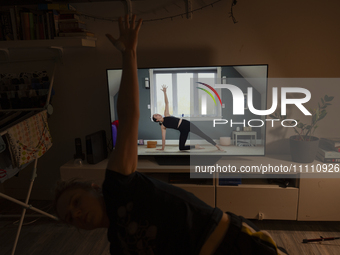 A woman is seen doing yoga exercises with YouTube trainer on a television in her living room in Warsaw, Poland on 23 March, 2024. (