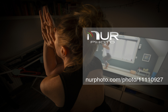 A woman is seen doing yoga exercises with YouTube trainer on a television in her living room in Warsaw, Poland on 23 March, 2024. 