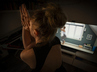 A woman is seen doing yoga exercises with YouTube trainer on a television in her living room in Warsaw, Poland on 23 March, 2024. (