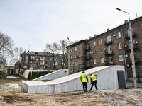 Two workers are constructing a new modular underground bomb shelter designed to accommodate 100 people in the yard of a five-story residenti...