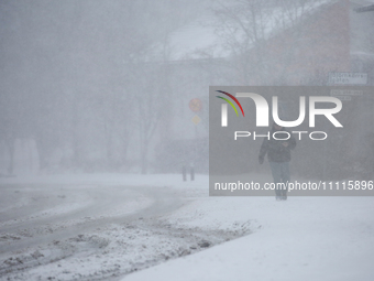 A man is walking along a road during a snowfall in Linkoping, Sweden, on April 2, 2024. (