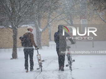 Two men are pushing bicycles along a road during a snowfall in Linkoping, Sweden, on April 2, 2024. (