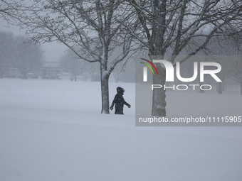 A man is walking along a road during a snowfall in Linkoping, Sweden, on April 2, 2024. (