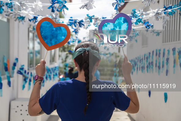 A woman is holding blue hearts made of cellophane paper while participating in a cultural activity as part of World Autism Awareness Day in...