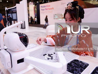 A woman is wearing traditional Chinese clothing and is playing Go with SenseRobot Go, a robot designed by SenseTime to play board games like...