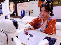 A woman is wearing traditional Chinese clothing and is playing Go with SenseRobot Go, a robot designed by SenseTime to play board games like...