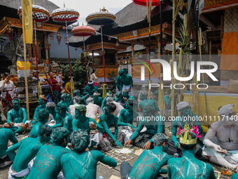 Balinese men with painted bodies are eating together as they attend the Ngerebeg tradition in Tegallalang Village, Bali, Indonesia, on April...