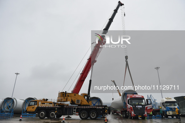 A crane is lifting wind turbine blades onto a special transport vehicle in Yangzhou, East China's Jiangsu province, on April 8, 2024. 