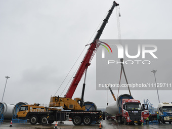 A crane is lifting wind turbine blades onto a special transport vehicle in Yangzhou, East China's Jiangsu province, on April 8, 2024. (