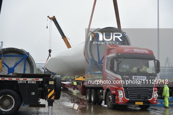 A crane is lifting wind turbine blades onto a special transport vehicle in Yangzhou, East China's Jiangsu province, on April 8, 2024. 