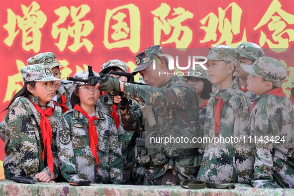 An instructor at a military experience camp is explaining the use of weapons to primary school students in Lianyungang, China, on April 13,...