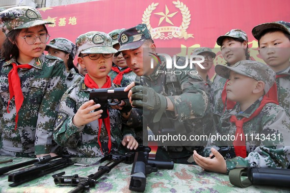 An instructor at a military experience camp is explaining the use of weapons to primary school students in Lianyungang, China, on April 13,...