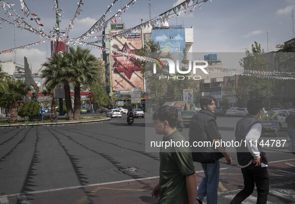 Young Iranian men are crossing a street while an anti-Israeli mural is visible on a wall in downtown Tehran, Iran, on April 13, 2024. The Pr...