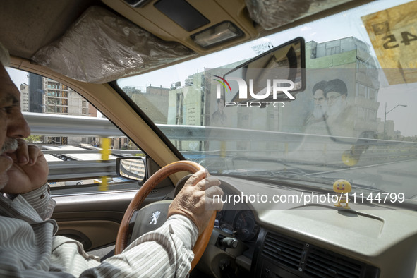 An Iranian taxi driver is driving past portraits of Iran's Supreme Leader Ayatollah Ali Khamenei (R), and the late Leader Ayatollah Ruhollah...