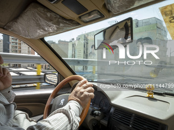 An Iranian taxi driver is driving past portraits of Iran's Supreme Leader Ayatollah Ali Khamenei (R), and the late Leader Ayatollah Ruhollah...