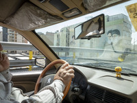 An Iranian taxi driver is driving past portraits of Iran's Supreme Leader Ayatollah Ali Khamenei (R), and the late Leader Ayatollah Ruhollah...