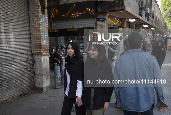 Two young Iranian women, who are not wearing mandatory headscarves, are walking together along a sidewalk near the Grand Bazaar in southern...