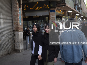 Two young Iranian women, who are not wearing mandatory headscarves, are walking together along a sidewalk near the Grand Bazaar in southern...