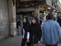 Two young Iranian women, who are not wearing mandatory headscarves, are walking together along a sidewalk near the Grand Bazaar in southern...