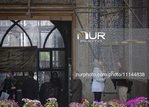 A young Iranian woman, who is not wearing a mandatory headscarf, is adjusting her scarf to enter the Grand Bazaar in southern Tehran, Iran,...