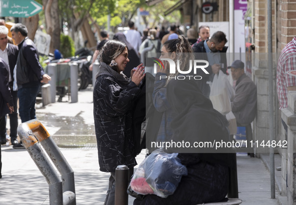 Two young Iranian women, who are not wearing mandatory headscarves, are speaking with each other while standing on a sidewalk near the Grand...