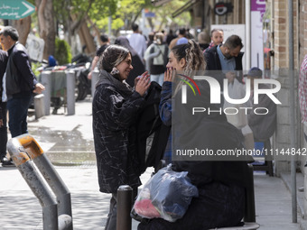 Two young Iranian women, who are not wearing mandatory headscarves, are speaking with each other while standing on a sidewalk near the Grand...