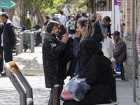 Two young Iranian women, who are not wearing mandatory headscarves, are speaking with each other while standing on a sidewalk near the Grand...