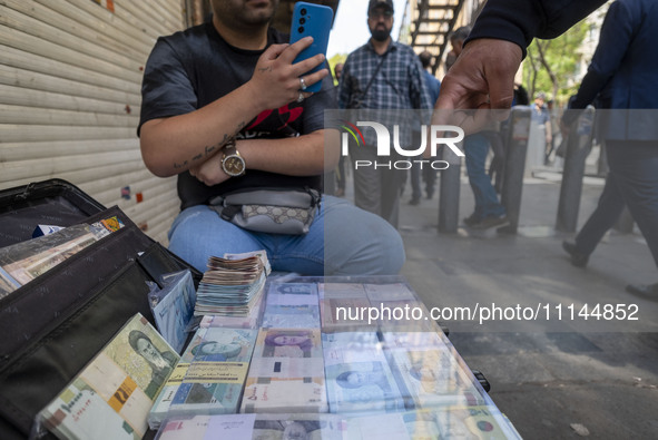 An Iranian street money changer is sitting on a sidewalk next to Iranian banknotes in Tehran's business district, Iran, on April 13, 2024. M...