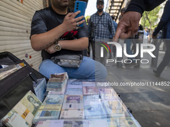 An Iranian street money changer is sitting on a sidewalk next to Iranian banknotes in Tehran's business district, Iran, on April 13, 2024. M...