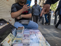 An Iranian street money changer is sitting on a sidewalk next to Iranian banknotes in Tehran's business district, Iran, on April 13, 2024. M...