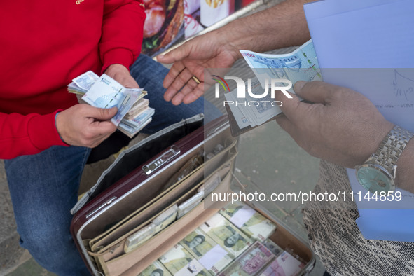 Two men are holding Iranian banknotes on a sidewalk in Tehran's business district, in Tehran, Iran, on April 13, 2024. Meanwhile, the Prime...