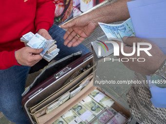 Two men are holding Iranian banknotes on a sidewalk in Tehran's business district, in Tehran, Iran, on April 13, 2024. Meanwhile, the Prime...