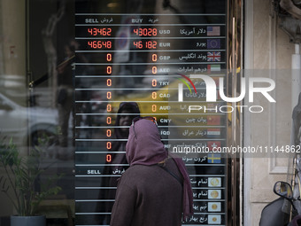 An Iranian woman is looking at an electronic board displayed at a currency exchange shop in Tehran's business district, in Tehran, Iran, on...