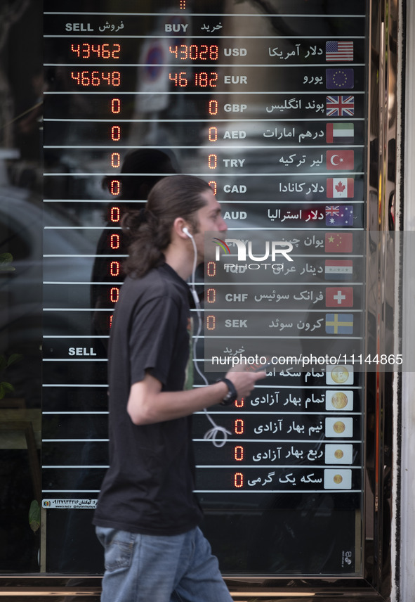 A young Iranian man is walking past an electronic board displayed at a currency exchange shop in Tehran's business district, Iran, on April...