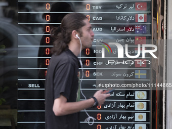 A young Iranian man is walking past an electronic board displayed at a currency exchange shop in Tehran's business district, Iran, on April...