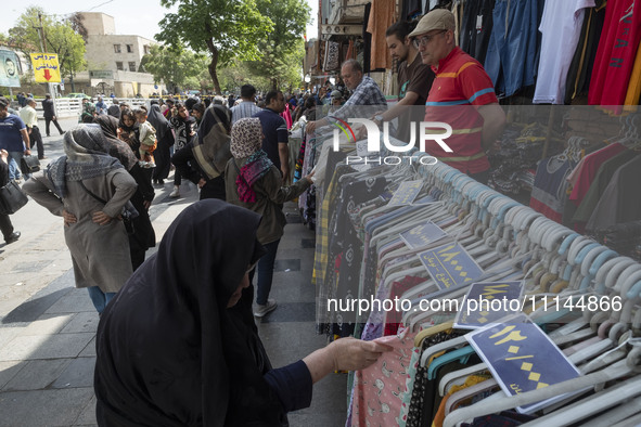 An elderly Iranian woman, veiled, is looking at dresses while shopping from a vendor near the Grand Bazaar in southern Tehran, Iran, on Apri...