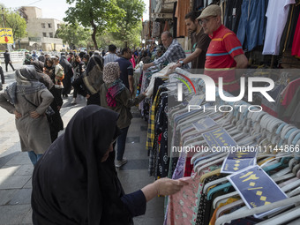 An elderly Iranian woman, veiled, is looking at dresses while shopping from a vendor near the Grand Bazaar in southern Tehran, Iran, on Apri...