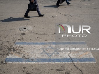 People are walking past an Israeli flag in downtown Tehran, Iran, on April 14, 2024. Iran is launching dozens of Unmanned Aerial Vehicles (U...