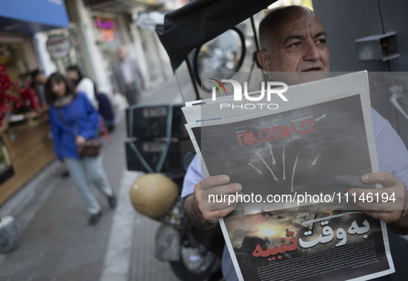 An Iranian man is sitting on a sidewalk in downtown Tehran, Iran, on April 14, 2024, holding a Jam-e Jam daily newspaper that features an il...